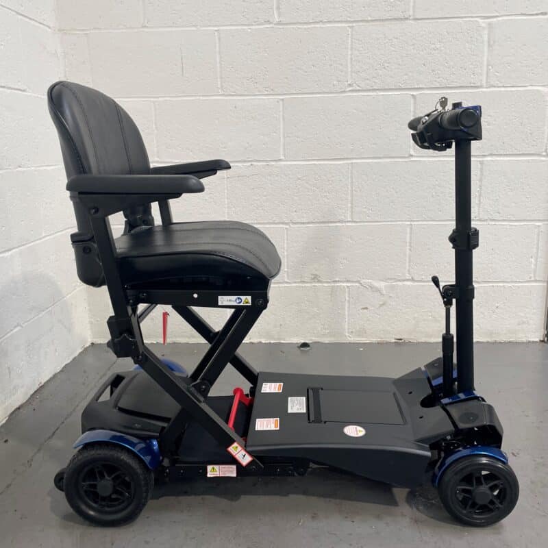 Right Side View of a Black and Dark Blue Drive Flex Automatic Folding Mobility Scooter. the Scooter Features a Sleek Design with a Comfortable, Black Leatherette Seat with a Backrest and Armrests. Below the Seat, the Scooter's Frame is Black with Red Safety Levers and Warning Labels. the Control Tiller is Tall with the Control Panel Fitted to the Top. It Stands on Solid Black Wheels with a Blue Trim That Complements the Overall Color Scheme. Drive Flex Autofold with Carry Case & off Board Charger