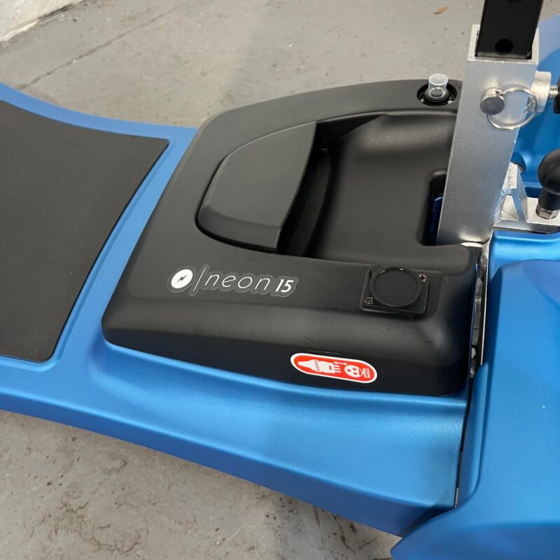 Close-up View of the Black Li-tech Neon 15 Lithium Lightweight Batter. the Battery is Housed in the Blue Chassis of the Scooter and Displays the Neon 15 Logo in White. an Easy to Access Handle is Positioned on the Top of the Battery to Allow It to Be Easily Removed. Li-tech Neon 15