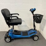 Right-hand Side View of a Li-tech Neon 15 Mobility Scooter Parked Indoors. the Scooter Has a Sleek Black and Blue Design with a High-backed, Black Leatherette Seat with Armrests. the Seat is Mounted Above a Blue Chassis with Black Anti-slip Foot Mats. Silver Rims on the Tires and a Front Wheel with Yellow Suspension Springs Are Visible, Indicating a Focus on Comfort and Stability. a Black Wire Basket is Attached to the Blue Tiller, Which Also Has a Simple Control Panel. Li-tech Neon 15
