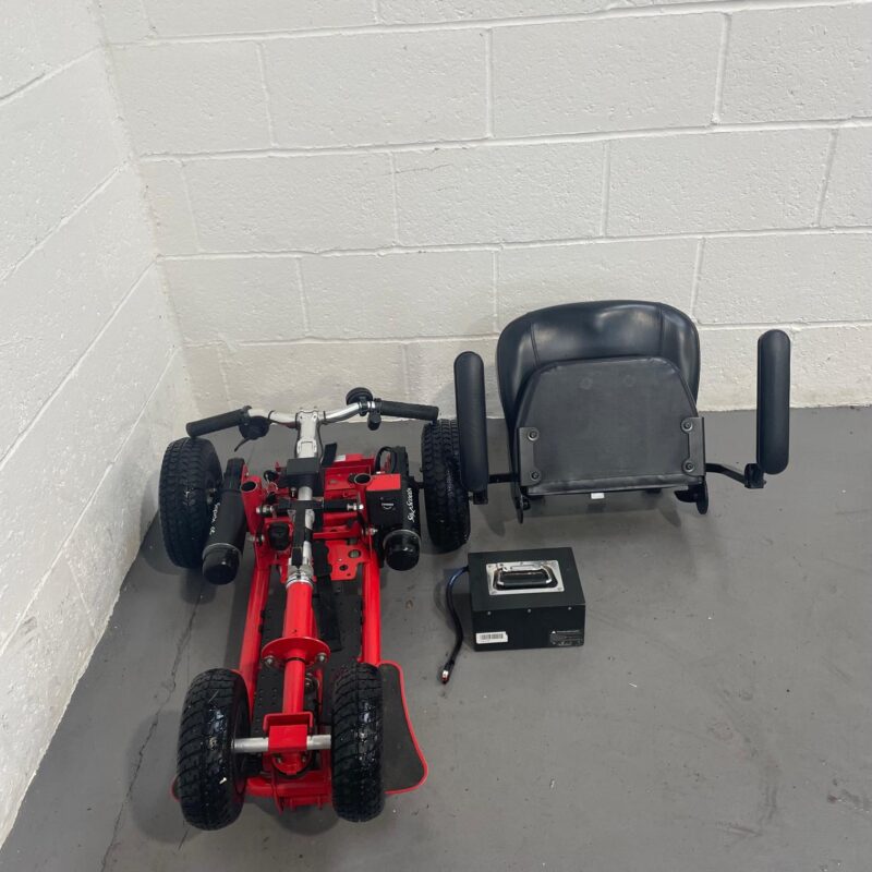View of the Deconstructed Parts of a Second-hand Three-wheeled Red Supascoota Sport Xl Mobility Scooter. It Shows the Folded Chassis, Rear-wheels, Seat and Battery As Separate Components. Supascoota Sport (lead Acid)