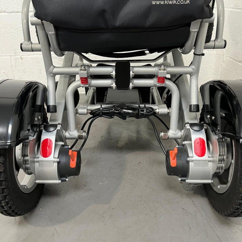 Close-up of the Rear of a Second-hand Silver and Black Kwk D09 Powerchair. There is a Handbrake on Each Rear Wheel to Allow the Chair to Free-wheel for Pushing. There is Also a Latch Under the Seat That Can Be Released to Allow the Chair to Fold Down. Kwk D09 Powerchair
