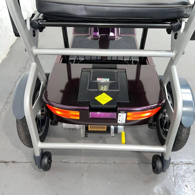 Close-up View of the Rear of a Purple 4mph Folding Second-hand One Rehab Q Fold Mobility Scooter. in View Are the Removable Lithium Battery, Reflectors and Stability Wheels. One Rehab Q Fold